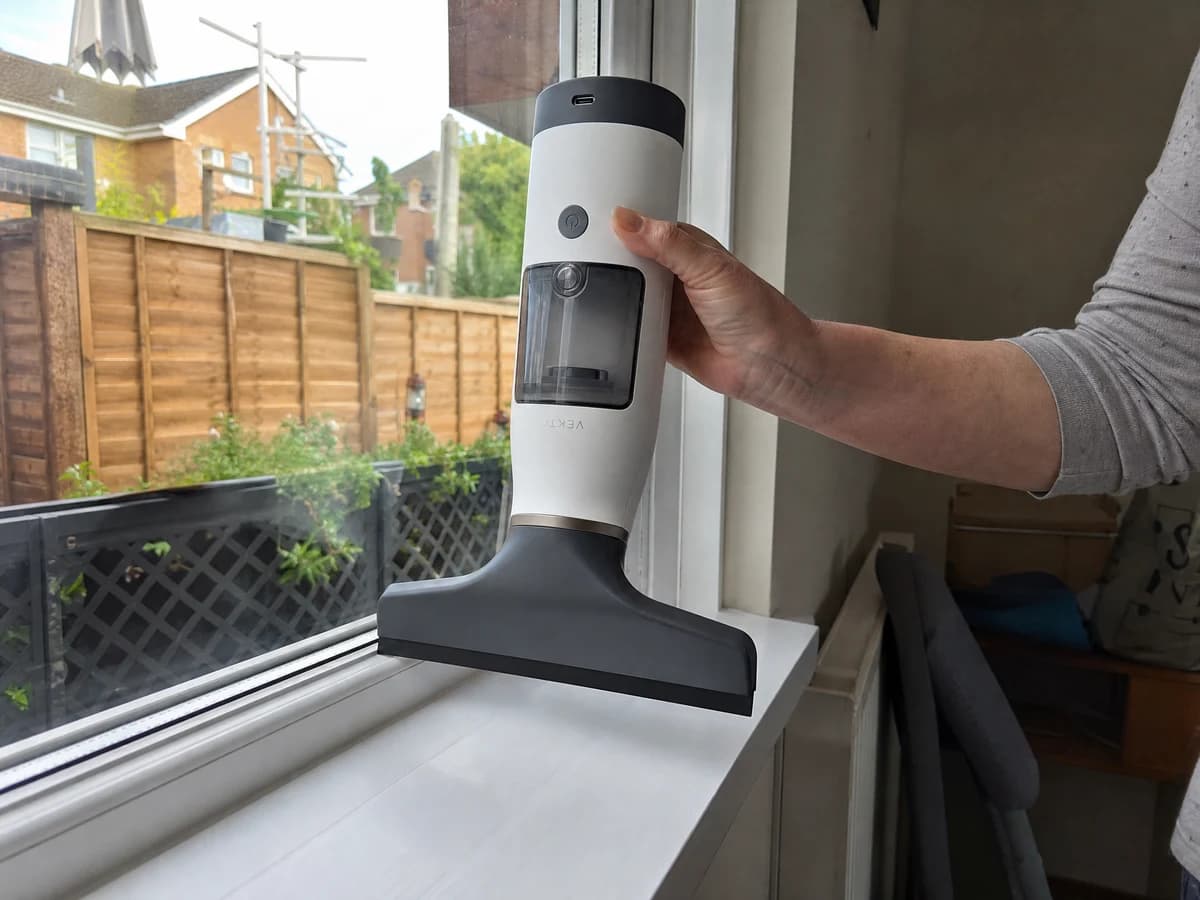 The Vekto Window Vac W10 held upside down along the bottom edge of a uPVC bedroom window above a dry white sill, the glass clear behind the blade