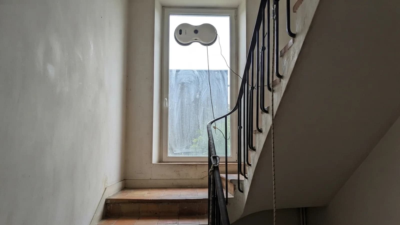 Le robot lave-vitre Vekto lave le haut d'une grande vitre de cage d'escalier, la corde descend vers la rampe