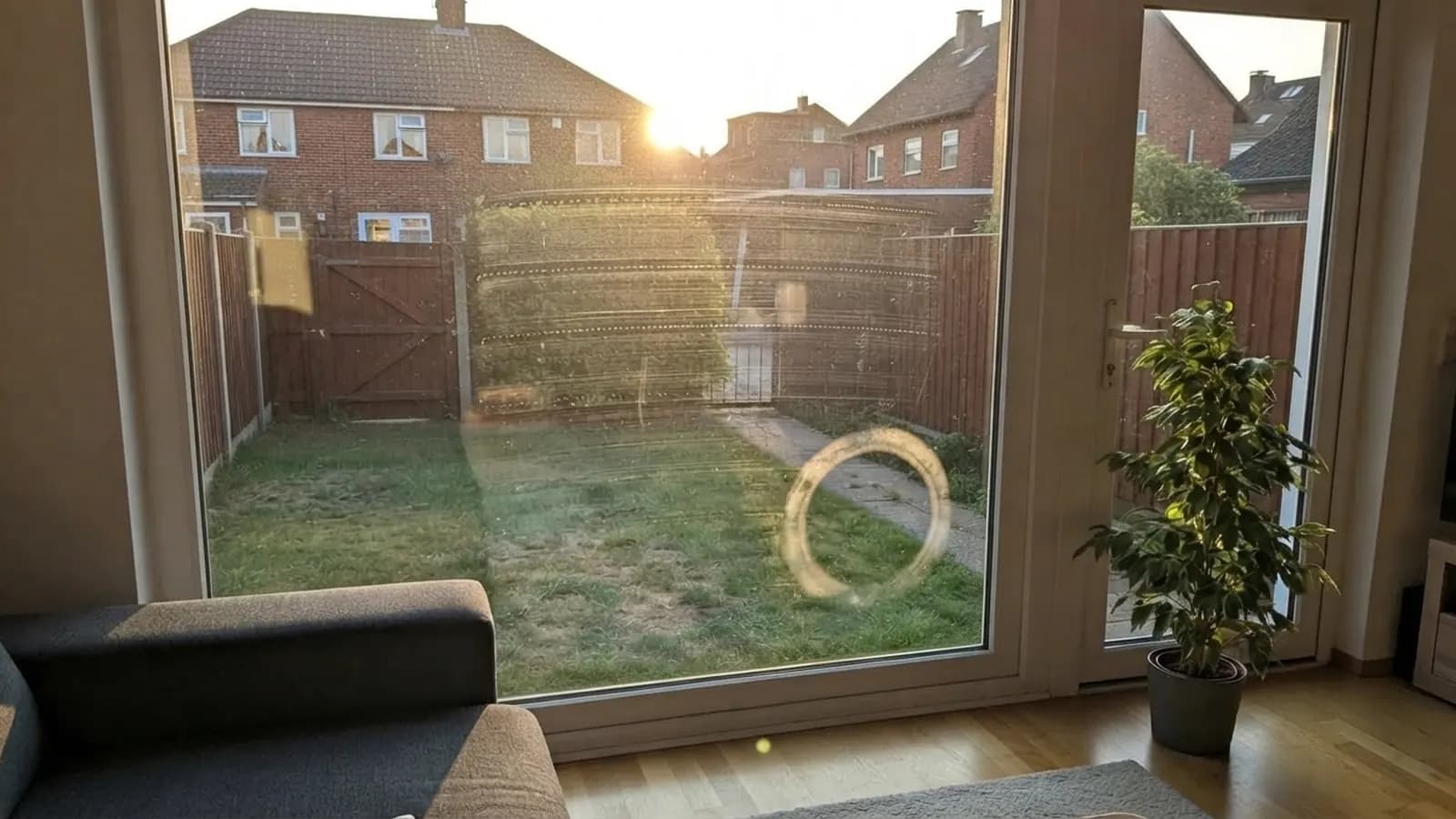 White uPVC patio doors with low evening sun shining through, faint horizontal streaks and a round swirl mark visible on the glass